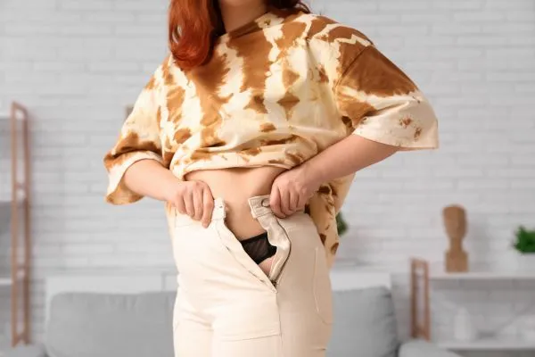 Image of woman trying to do her trousers up after pregnancy weight gain Greenford